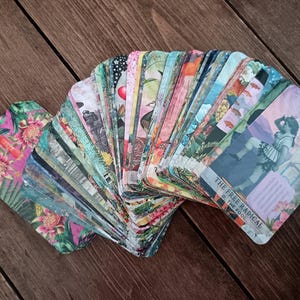 May include: A deck of tarot cards fanned out on a wooden surface. The cards feature colorful illustrations with floral, botanical, and figurative designs. One card displays the text "THE FREE RADICAL O THE FOOL."