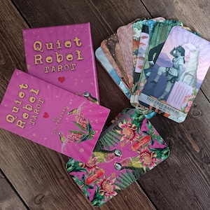 Può includere: Un set di tarocchi con una scatola rosa e carte abbinate. La scatola e i dorsi delle carte riportano "Quiet Rebel Tarot" in lettere dorate. Le carte presentano illustrazioni e il testo "The Free Radical & The Pool". È incluso anche un astuccio con motivi floreali.