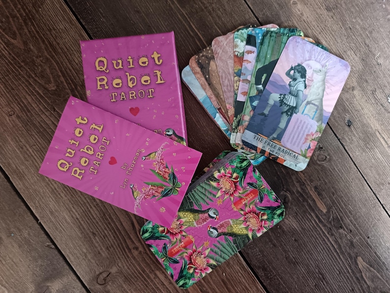 May include: A tarot card set with a pink box and matching cards. The box and card backs read "Quiet Rebel Tarot" in gold lettering. The cards feature illustrations and the text "The Free Radical & The Pool". A floral patterned pouch is also included.