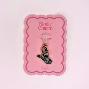 May include: A black and gold charm with a wizard hat design and the text "WIZARD IN TRAINING" on a pink card that says "Kindle Charm". The charm has a gold-coloured clasp.