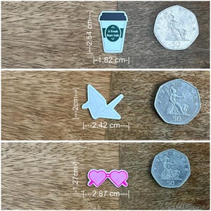 May include: Three decorative charms: a light blue coffee cup with "A Fresh Start Cafe" text (1.82 cm x 2.54 cm), a light blue origami crane (2.42 cm x 2 cm), and pink heart-shaped sunglasses (2.87 cm x 1.27 cm).