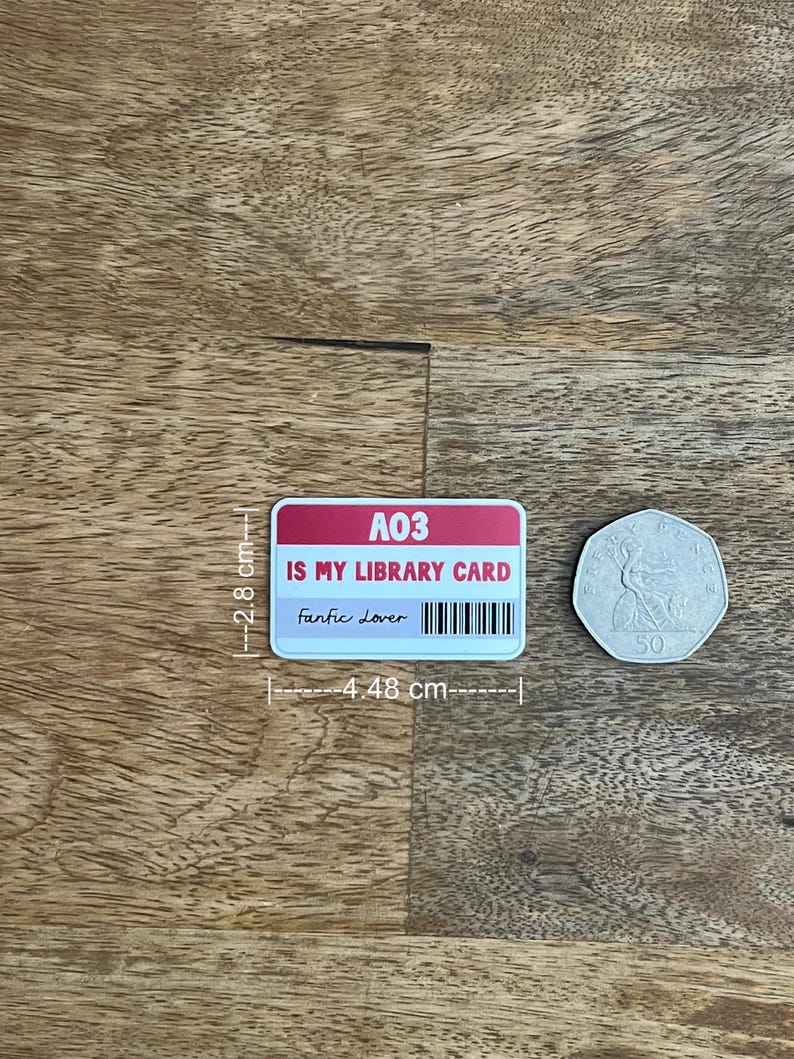 May include: A rectangular sticker with the text "A03 IS MY LIBRARY CARD Fanfic Lover" and a barcode. The sticker is 4.48 cm wide and 2.8 cm tall. A 50 pence coin is next to the sticker.