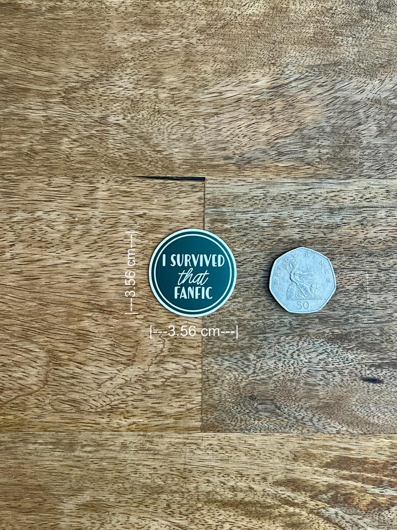 May include: A round sticker, 3.56 cm in diameter, with the text "I SURVIVED that FANFIC" in white on a dark green background. A 50-cent coin is next to the sticker. The sticker is on a wooden surface.