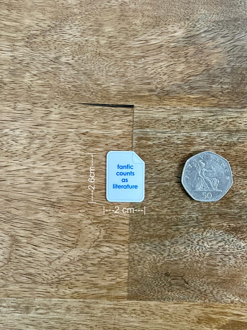 May include: A light blue sticker, 2.6 cm tall and 2 cm wide, with the text "fanfic counts as literature". A 50-cent coin is next to the sticker. The sticker and coin are on a wooden surface.