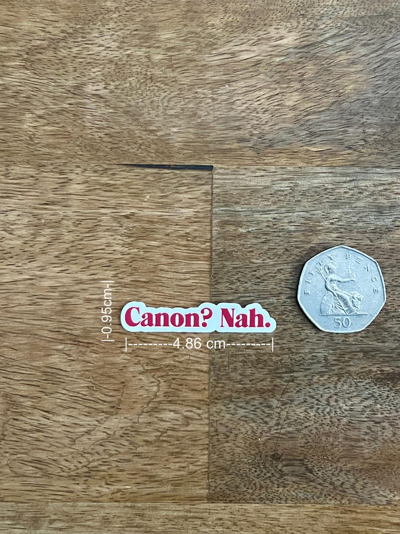 May include: A white sticker with the text "Canon? Nah." in pink lettering. The sticker is 0.37 inches tall and 1.91 inches wide. A 50-cent coin is next to the sticker on a wooden surface.