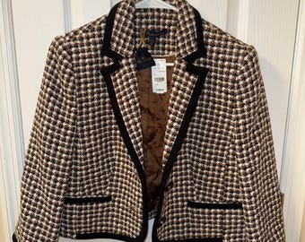 Könnte beinhalten: Braune und weiße karierte Blazerjacke mit schwarzem Besatz und Reverskragen. Die Jacke hat einen Zwei-Knopf-Verschluss und zwei Vordertaschen. Der Blazer hängt an einem weißen Kleiderbügel vor einer weißen Tür.