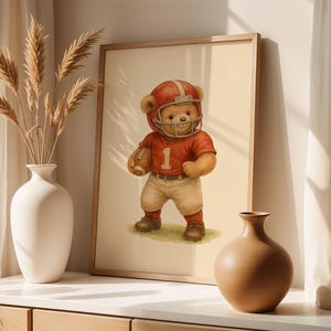 Pu&ograve; includere: Un'illustrazione incorniciata di un orsacchiotto che indossa una divisa da football rosso e bianca e un casco. L'orso tiene un pallone da football e sta in piedi su uno sfondo beige.