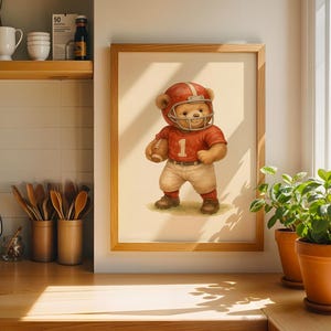 Pu&ograve; includere: Un'illustrazione incorniciata di un orsacchiotto che indossa una divisa da football rosso e bianca e un casco. L'orso tiene un pallone da football e sta in piedi su un campo verde. L'illustrazione &egrave; su uno sfondo bianco.