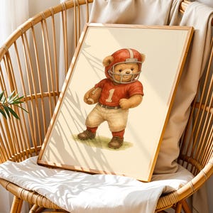 Pu&ograve; includere: Un'illustrazione ad acquerello di un orsacchiotto che indossa una divisa da football rosso e bianca e un casco, tenendo un pallone da football. L'orso &egrave; in piedi su un campo verde.