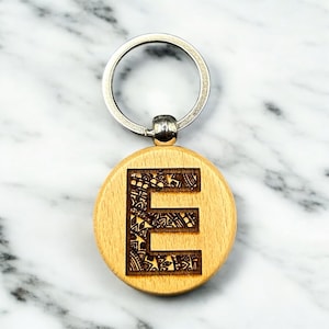 May include: Wooden keychain with a silver key ring and a round wooden charm with the letter "E" engraved in a decorative pattern.