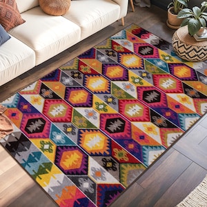 May include: A colourful geometric patterned rug with a white sofa, cushions, and plants. The rug features a vibrant mix of colours including yellow, pink, blue, and black. The room has a dark wall and a large window.
