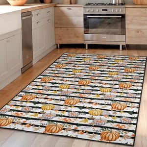 May include: A rectangular kitchen rug with a black and white striped pattern. The rug features a repeating design of pumpkins in shades of orange, yellow, and gray, along with autumn leaves. The rug is placed on a wooden floor in a kitchen setting.