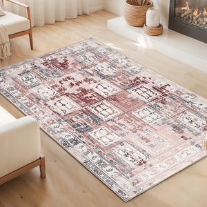 Pode incluir: Um tapete retangular com um design desgastado de inspiração vintage. O tapete apresenta um padrão de quadrados em tons de vermelho, branco e cinza, com uma borda. O tapete está colocado sobre um chão de madeira numa sala de estar.