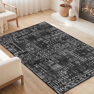 Puede incluir: Una alfombra rectangular en blanco y negro con un patrón geométrico. La alfombra presenta un diseño desgastado con líneas y formas blancas sobre un fondo oscuro. Se coloca sobre un suelo de madera clara. La alfombra es el punto focal de la habitación.
