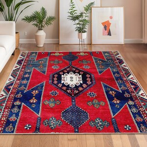May include: A rectangular red area rug with a geometric pattern in blue, white, and green. The rug features a central medallion design and borders with repeating motifs. This rug is suitable for living rooms and bedrooms.