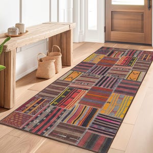 Könnte beinhalten: Ein rechteckiger Patchwork-Teppich mit einer Vielzahl von Farben und Mustern. Der Teppich hat Quadrate in Rot, Gelb, Orange und Schwarz. Der Teppich liegt auf einem Holzboden in einem Flur.