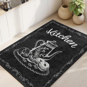 Könnte beinhalten: Schwarzer rechteckiger Küchenteppich mit einer weißen Kreide-Illustration einer Teekanne, Donuts und dem Wort "Kitchen". Der Teppich hat einen dekorativen Rand und liegt auf einem hellen Holzboden.