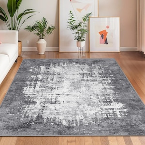 Könnte beinhalten: Rechteckiger Teppich mit einem verwitterten, abstrakten Design. Der Teppich hat eine Mischung aus Grau- und Weißtönen, die ein strukturiertes Aussehen erzeugen. Er liegt auf einem Holzboden und ist von einem weißen Sofa, Pflanzen und Kunstwerken umgeben.