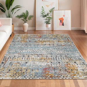 Può includere: Un tappeto rettangolare con un design vintage e usurato. Il tappeto presenta un mix di colori, tra cui blu, giallo, arancione e nero, creando un motivo strutturato. È posizionato su un pavimento in legno in un ambiente soggiorno.