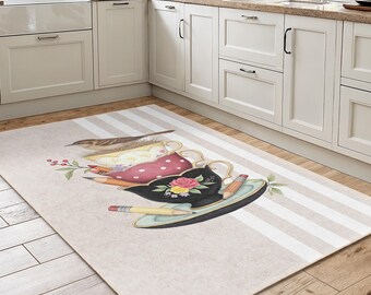 May include: A rectangular kitchen rug with a whimsical teacup design. The rug features a beige background with white stripes and illustrations of teacups, pencils, and a bird. The teacups are in various colors, including red, black, and yellow.