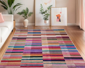 May include: A colorful rectangular rug with a geometric pattern of horizontal stripes in various colors, including pink, purple, blue, and green. The rug is placed on a hardwood floor in a living room setting.