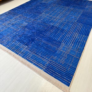 May include: A blue and gray patterned rug with a fringe border. The rug has a geometric design with stripes and squares.