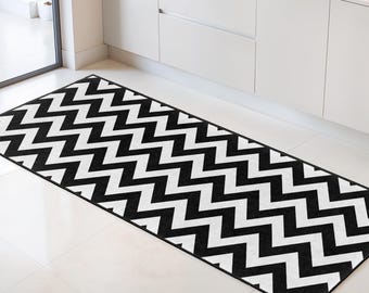 May include: A black and white chevron patterned kitchen rug. The rug is rectangular and lies on a white tile floor. The zig-zag pattern is a classic design element, adding a modern touch to the kitchen space. The rug is placed in front of the kitchen cabinets.