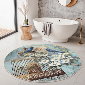 May include: Round area rug with a birdcage design. The rug features two blue birds perched on a cage with white flowers and a light blue background. The rug is placed in a bathroom setting.