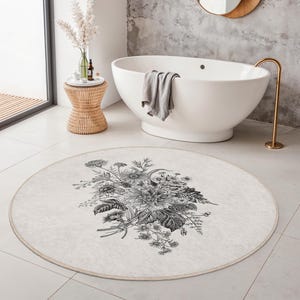 May include: A circular rug in cream with a black and white floral pattern. The rug is on a white tiled floor in a bathroom. The edge of the rug has a light beige border. The rug's diameter is approximately 150 cm.