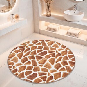 May include: A circular bathroom rug with a giraffe print. The rug has a white base with irregular brown and tan shapes, forming a spotted pattern. The rug is positioned on a white tiled floor.