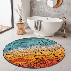 Op de afbeelding: Een ronde, kleurrijke vloerkleed met een abstract ontwerp. Het vloerkleed heeft een kleurengradiënt van blauw, oranje en geel, met zwarte dierensilhouetten en geometrische patronen. Het ligt op een witte tegelvloer.