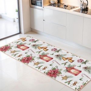 Könnte beinhalten: Ein rechteckiger Küchenteppich mit festlichem Weihnachtsmotiv. Der Teppich hat einen weißen Hintergrund mit sich wiederholenden Mustern aus roten Laternen, Weihnachtssternen, goldenen Sternen, Zuckerstangen und Glocken. Der Teppich ist etwa 152 cm lang.