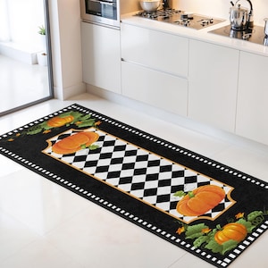 Könnte beinhalten: Rechteckiger Küchenteppich mit schwarzem Rand und weißem Punktmuster. Die Mitte hat ein schwarz-weißes Schachbrettmuster. Orangefarbene Kürbisse mit grünen Blättern sind auf dem Teppich platziert und schaffen ein Herbstthema.