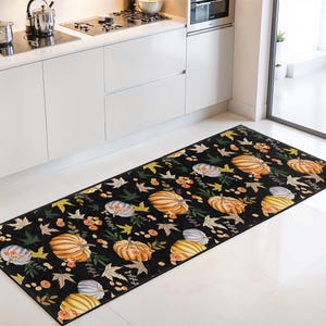 Könnte beinhalten: Ein schwarzer Küchenläufer mit einem sich wiederholenden Muster aus orangefarbenen, gelben und grauen Kürbissen, durchsetzt mit Herbstblättern und Beeren. Der rechteckige Teppich liegt vor einer weißen Küchenzeile und ist etwa 200 cm lang.