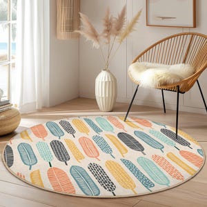 May include: A round area rug with a cream background and a repeating pattern of colorful feather shapes. The feathers are in shades of orange, blue, yellow, and gray. The rug is placed on a wooden floor.