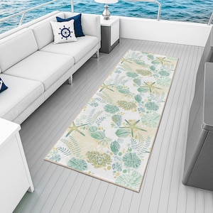 Könnte beinhalten: Ein rechteckiger Teppich mit nautischem Thema, mit einem Muster aus Seesternen, Muscheln und Wasserpflanzen in Grün-, Beige- und Weißtönen. Der Teppich liegt auf einem Bootsdeck, mit einem weißen Sofa und blauem Meer im Hintergrund.