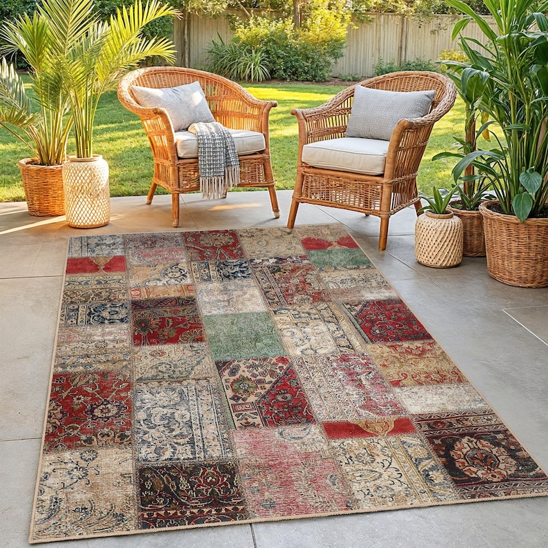 Peut inclure: Un tapis rectangulaire en patchwork avec une bordure beige. Le tapis pr&eacute;sente une vari&eacute;t&eacute; de carr&eacute;s &agrave; motifs dans des tons de rouge, beige, bleu et vert. Deux chaises en osier avec coussins et oreillers sont en arri&egrave;re-plan.