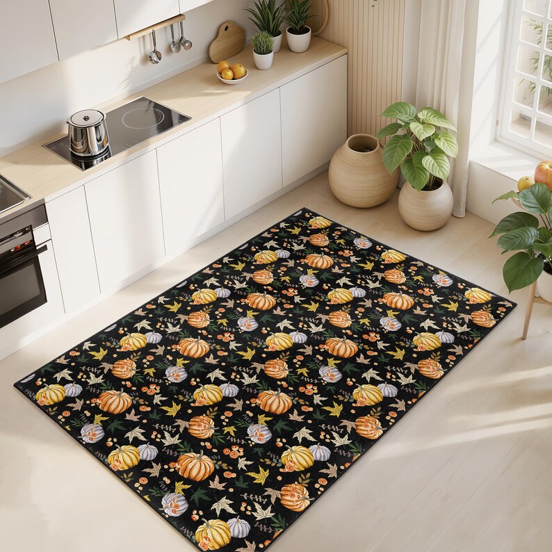 Puede incluir: Alfombra rectangular negra con un patr&oacute;n repetido de calabazas en tonos naranja, amarillo y blanco, intercaladas con hojas y bayas verdes y amarillas. La alfombra est&aacute; en un entorno de cocina.