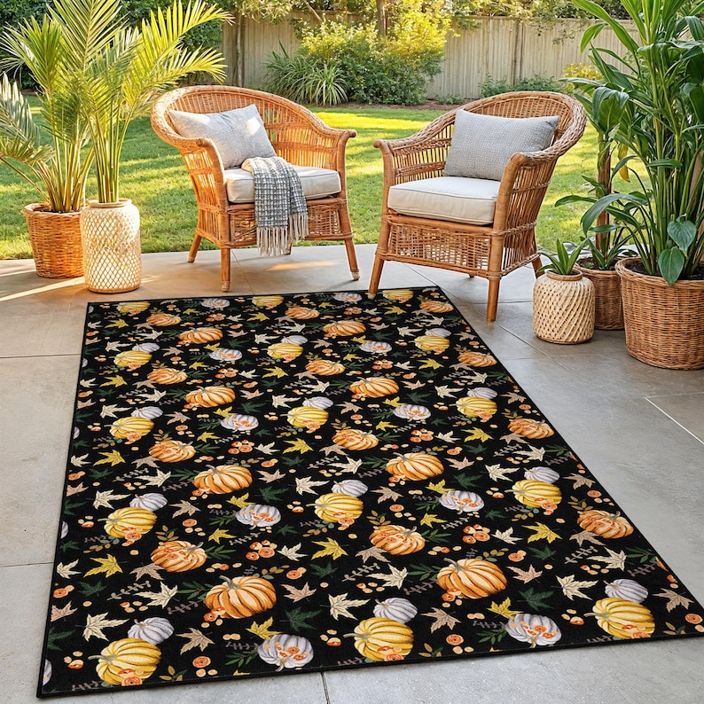 Puede incluir: Alfombra rectangular negra para exteriores con un patr&oacute;n repetido de calabazas, hojas y bayas en tonos naranja, amarillo y blanco. La alfombra est&aacute; colocada en un patio con sillas de mimbre y plantas en macetas.