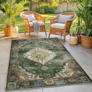 May include: A rectangular green area rug with a distressed, vintage-inspired design. The rug features a central medallion pattern in cream, blue, and yellow, surrounded by a border of darker green and blue. Two wicker chairs are in the background.