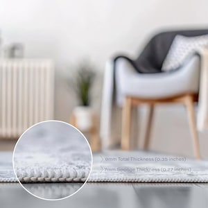 May include: Close-up of a light-colored rug with a detailed edge. The total thickness is 0.35 inches, with a 0.27-inch sponge thickness. The rug is on a dark wooden floor, with a blurred background of a chair and a plant.