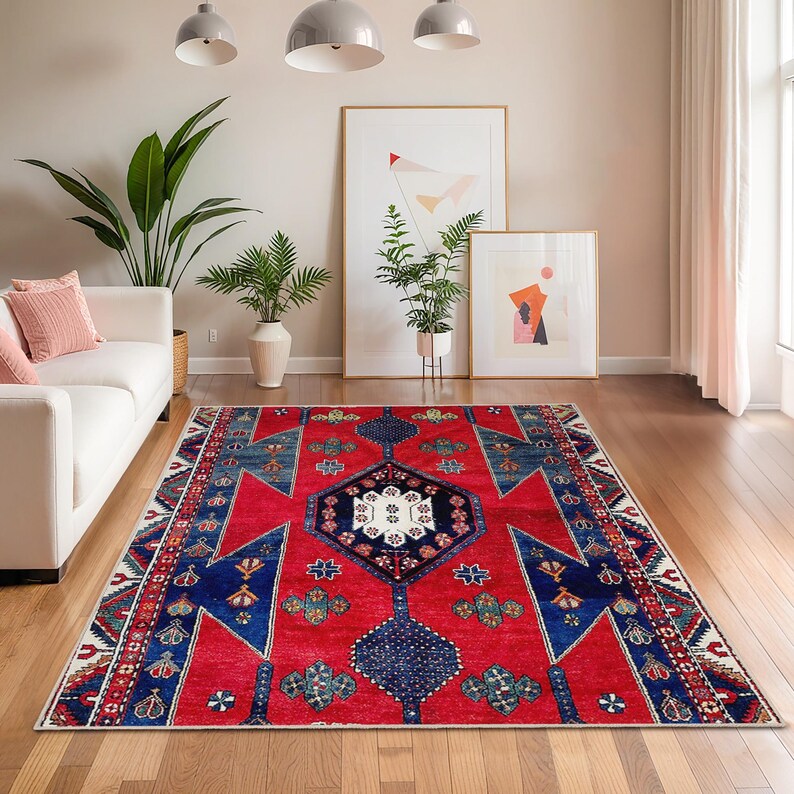 May include: A rectangular red area rug with a geometric pattern in blue, white, and green. The rug features a central medallion design and borders with repeating motifs. This rug is suitable for living rooms and bedrooms.