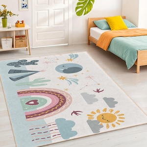 Könnte beinhalten: Rechteckiger Teppich mit einem skurrilen Design mit Regenbogen, Sonne, Mond, Sternen, Wolken und einem Kaktus. Der Teppich hat einen hellblauen Rand und einen cremefarbenen Hintergrund. Das Design ist in sanften Pastellfarben gehalten.