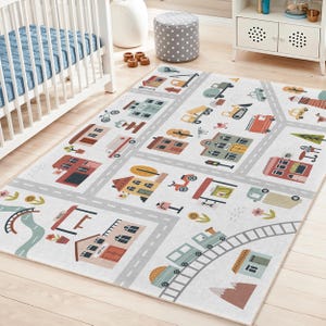 May include: A white children's play rug with a town design. The rug features gray roads, colorful houses, trees, and vehicles. A train travels along a track. The rug is designed for a nursery or playroom.