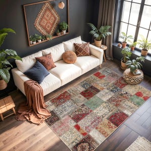 Peut inclure: Un tapis patchwork multicolore avec divers motifs, dont du rouge, beige et vert, est pos&eacute; sur un sol en bois. Le tapis se trouve dans un salon avec un canap&eacute; blanc, des coussins et des plantes en pot.