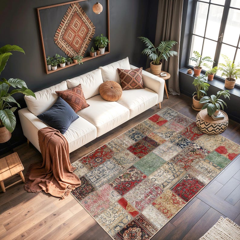 Peut inclure: Un tapis patchwork multicolore avec divers motifs, dont du rouge, beige et vert, est pos&eacute; sur un sol en bois. Le tapis se trouve dans un salon avec un canap&eacute; blanc, des coussins et des plantes en pot.