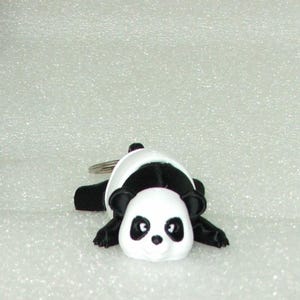 May include: A black and white panda bear keychain with a silver ring. The panda is lying on its belly with its paws outstretched.