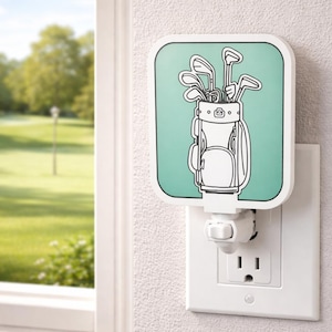 May include: A golf-themed night light featuring a white golf bag and clubs on a teal background. The night light plugs into a standard electrical outlet. The design is outlined in black.