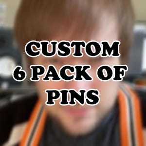 May include: The image shows the text "CUSTOM 6 PACK OF PINS" in a bold, black font with a white outline. The text is centered, likely advertising custom pins. The background is blurred.