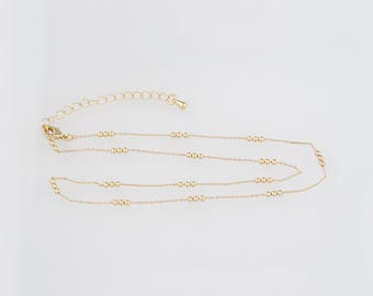 May include: Delicate gold-colored necklace with small, evenly spaced beads. The necklace has a fine chain and an adjustable clasp. The design is simple and elegant, suitable for layering or wearing alone. The necklace is displayed on a white background.